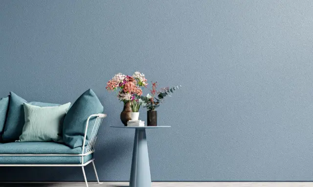 Divano blu e un tavolino con fiori su una parete azzurra, un'idea per pareti colorate particolari che crea un'atmosfera rilassante.