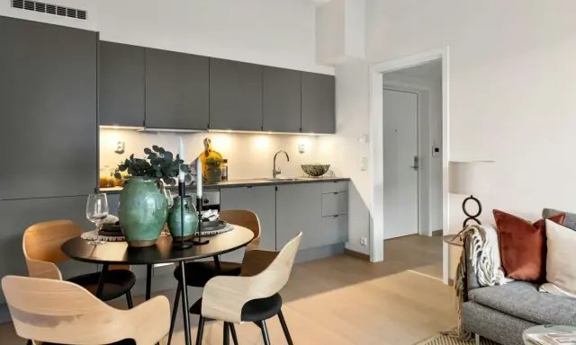Arredare una sala moderna con cucina a vista: tavolo rotondo con sedie in legno, vasi verdi e candele.