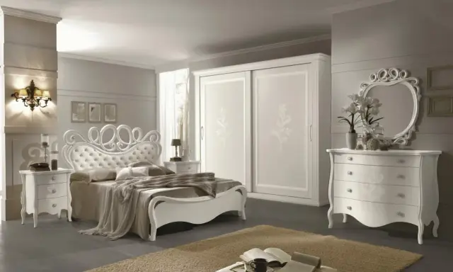 Elegante camera da letto bianca con letto capitonné, armadio scorrevole e comò con specchio. Ottime idee camera da letto bianca per un ambiente raffinato.