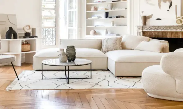 Un soggiorno luminoso con divani e design moderno. Un divano componibile bianco, una poltrona bouclé e una sedia grigia su un tappeto geometrico.