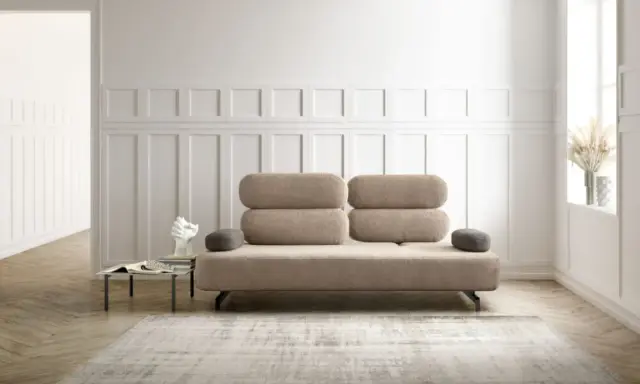 Un elegante divano beige, un'opera d'arte di design, domina la scena. Accanto, un tavolino con libri e una scultura moderna.