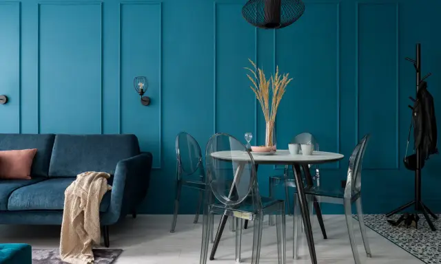 Soggiorno moderno con divano blu, tavolo rotondo con sedie trasparenti e pareti color ottanio.
