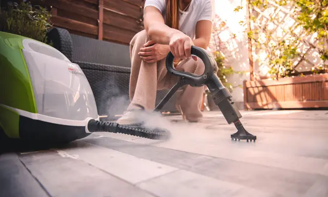 Persona usa un vaporetto per pulire la moquette esterna, creando una nuvola di vapore.