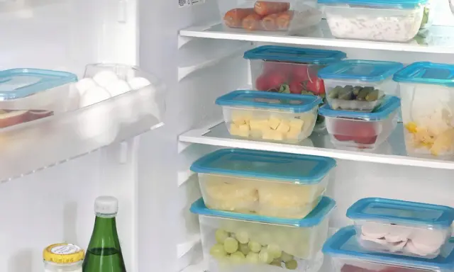 Frigo organizzato con contenitori trasparenti: carote, formaggio, cetrioli, uva, affettati. Un esempio di come organizzare il frigo per conservare al meglio gli alimenti.