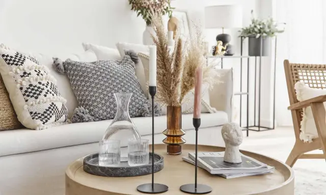 Un accogliente salotto bohemien con cuscini decorativi, un vaso di erba della pampa e candele su un tavolino rotondo.