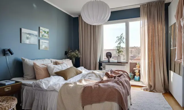 Accogliente camera da letto blu e beige con letto comodo, quadri astratti e grande finestra luminosa.