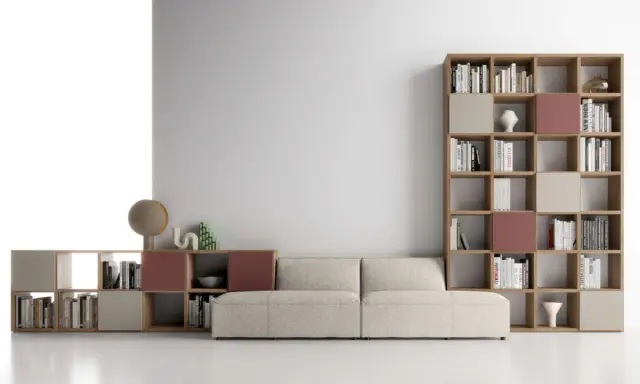 Un comodo divano beige è posizionato davanti a una libreria modulare in legno, con libri e oggetti decorativi.