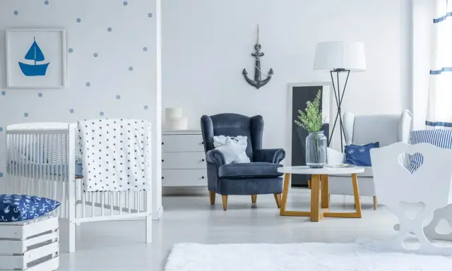 Un accogliente salotto stile marinaro con culla, poltrona blu e decorazioni a tema nautico.