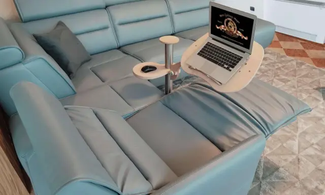 Comodo tavolino porta pc in legno e metallo, agganciato a un divano in pelle azzurra, con laptop aperto e mouse.