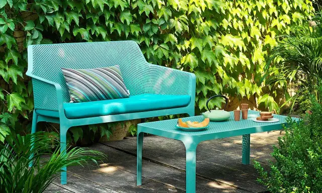 Divano e tavolino Nardi Spa Chiampo in un giardino rigoglioso, con cuscini color acqua e un set da tè.