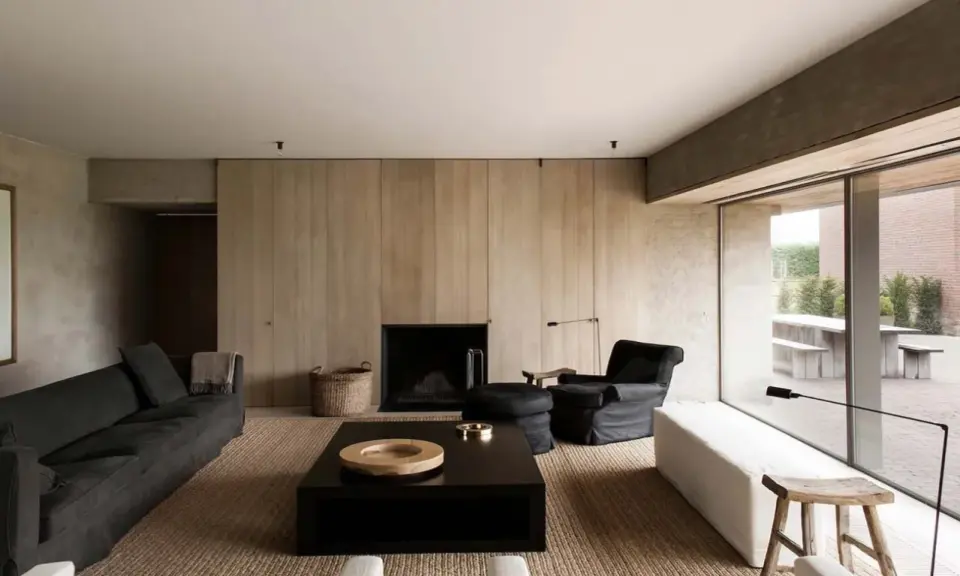 Elegante salone moderno con divani scuri, camino a parete in legno, tavolino nero e poltrona. Un esempio di come arredare un salone con stile minimalista.