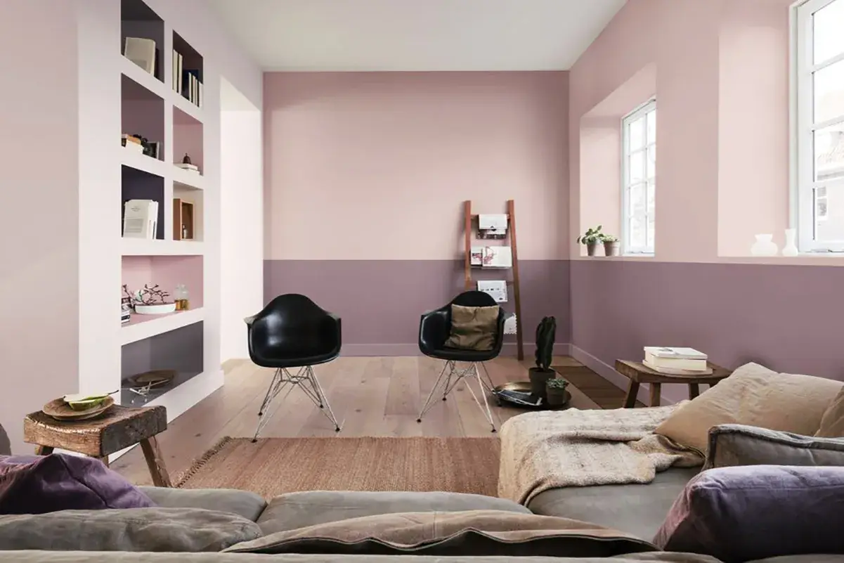 Soggiorno moderno con pareti bicolore color malva e rosa cipria, due sedie nere, divano e scaffalatura a muro.
