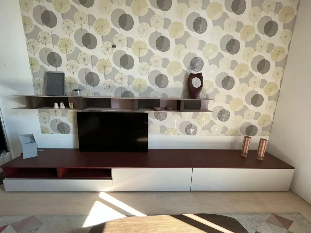 Mobile TV moderno con ante bianche e piano bordeaux, su carta da parati con motivi a soffione. Un portal Calligaris che arreda con stile.
