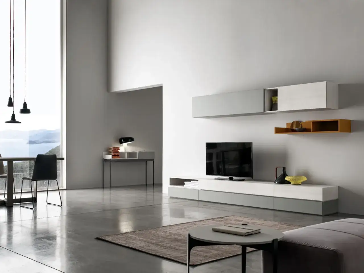 Elegante salotto grigio e bianco con mobili sospesi, TV e un tavolino. Vista su un paesaggio marino da un'ampia finestra.