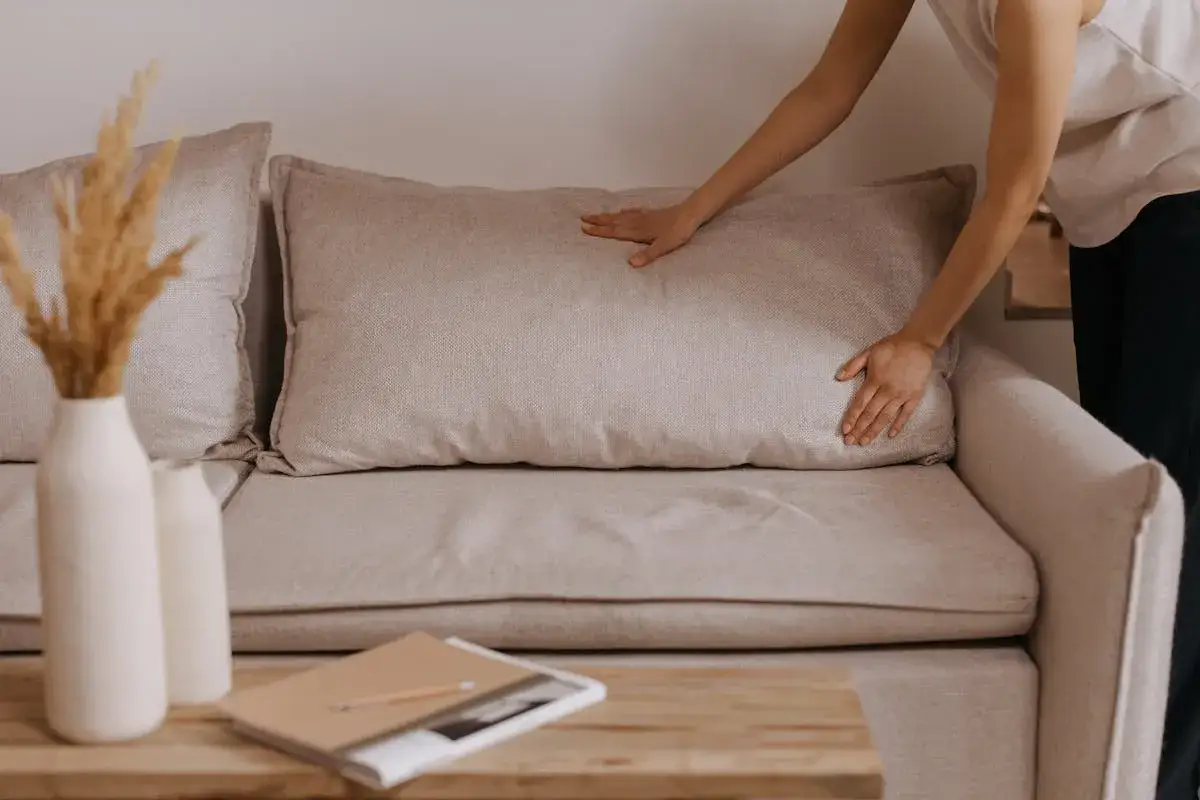 Mani che sistemano un cuscino su un divano beige, un'idea per come foderare un divano fai da te.
