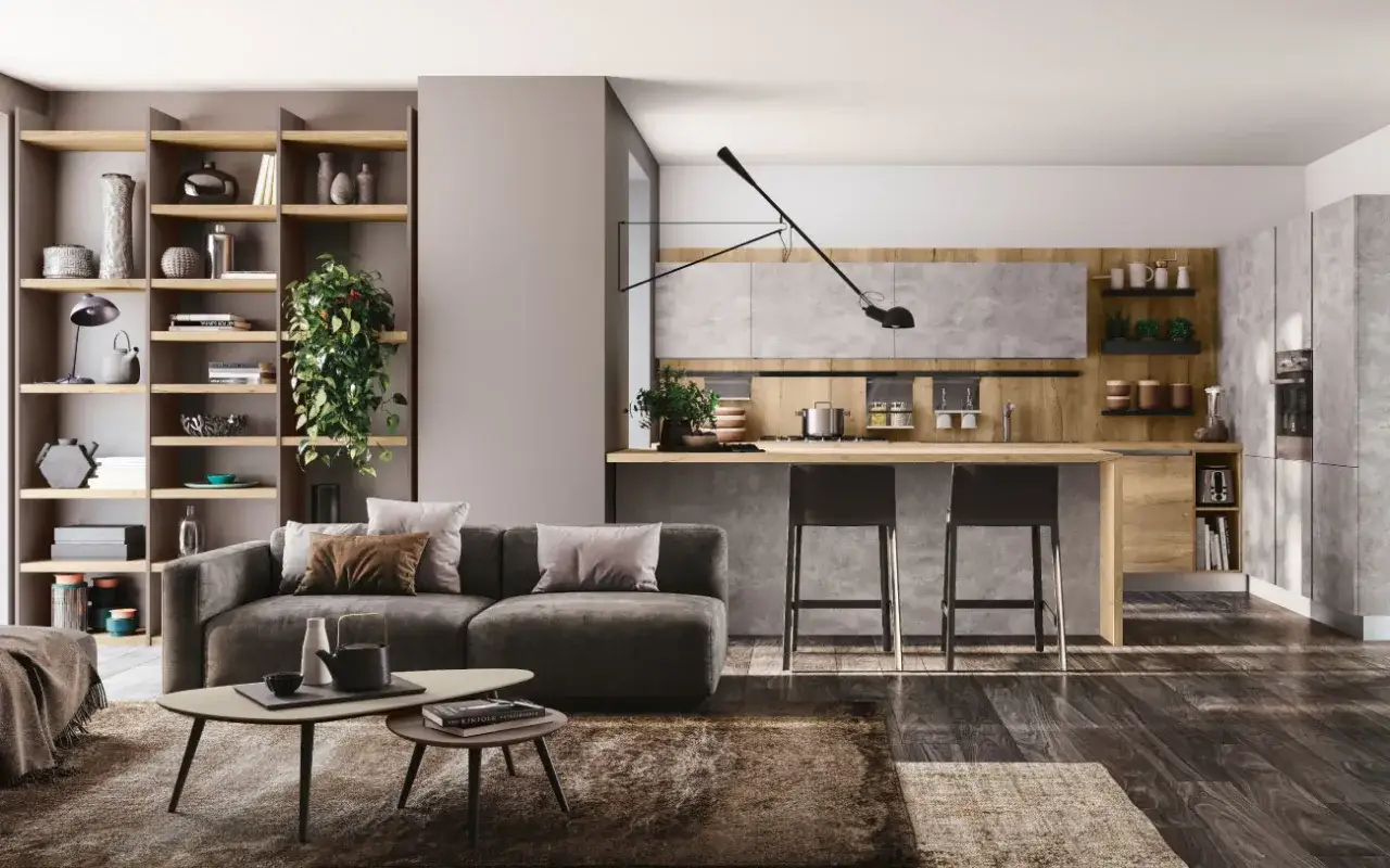 Elegante zona giorno con divano antracite, tavolini asimmetrici e cucina moderna con isola centrale. Scaffali a vista pieni di oggetti decorativi.
