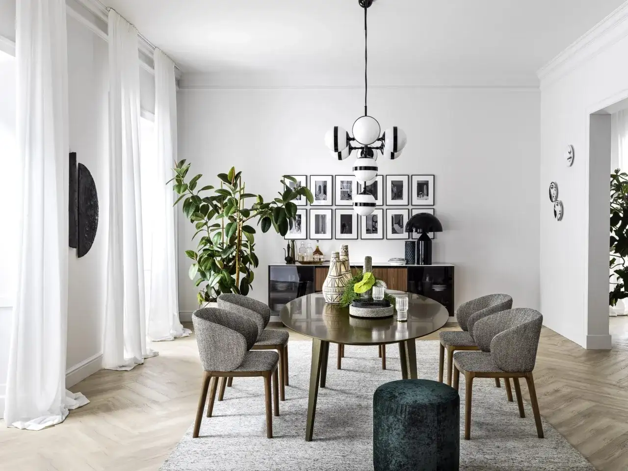 Eleganza moderna per arredare sala da pranzo: tavolo ovale, sedie grigie, credenza nera e lampadario di design.