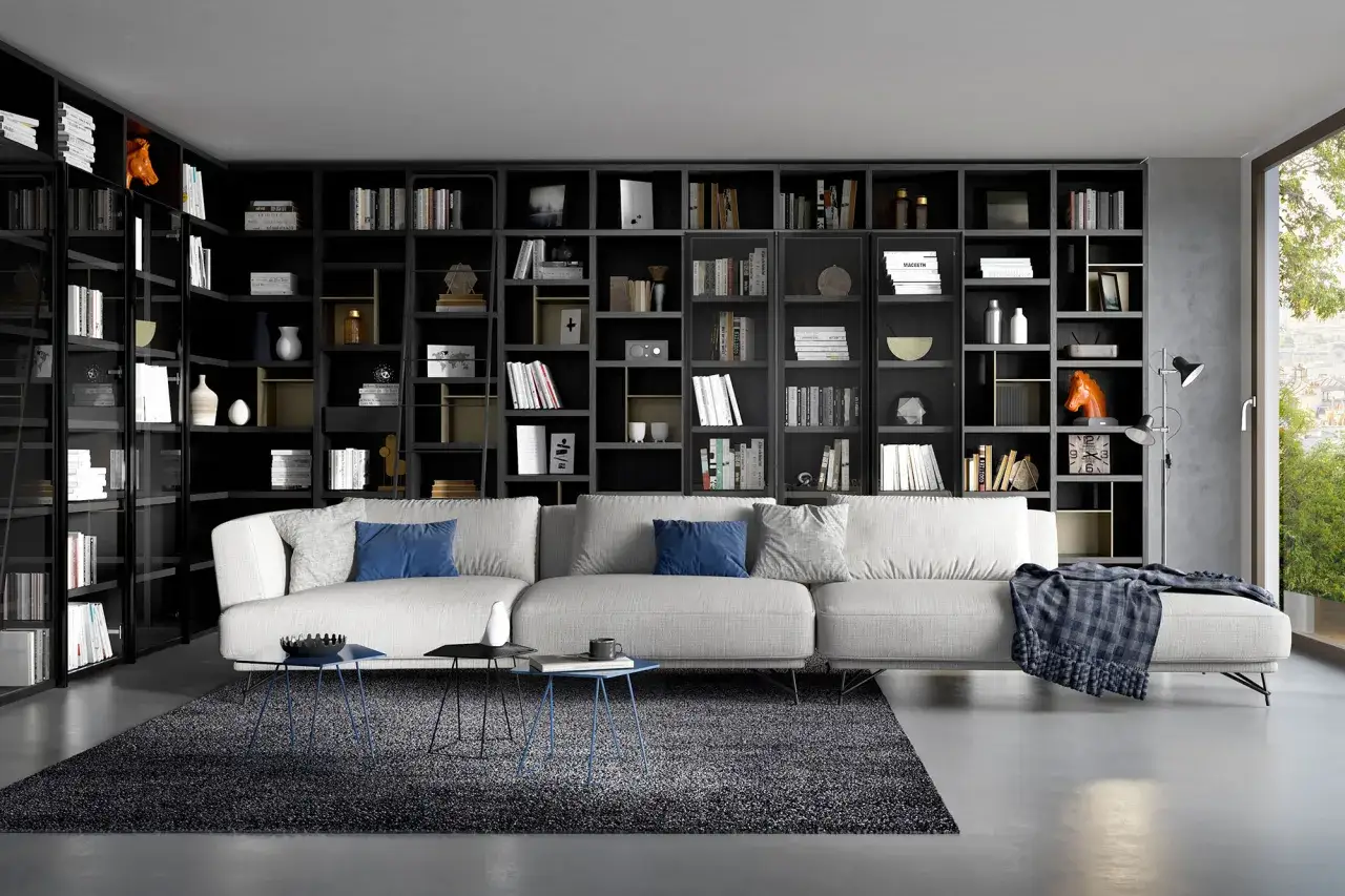 Un ampio divano bianco davanti a una libreria nera piena di libri e oggetti decorativi.