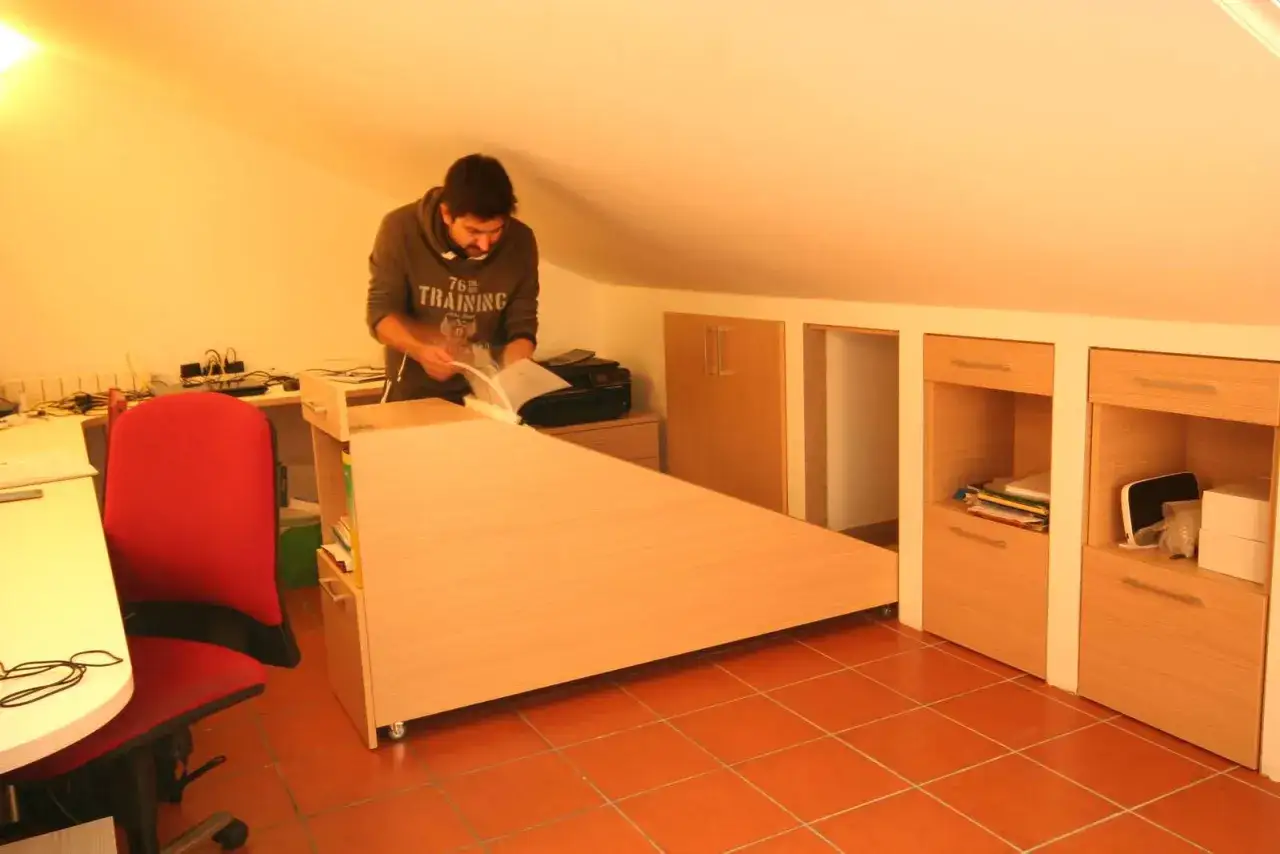 Uomo in mansarda con idee sottotetto molto basso: scrivania angolare, armadi a muro e sedia rossa.