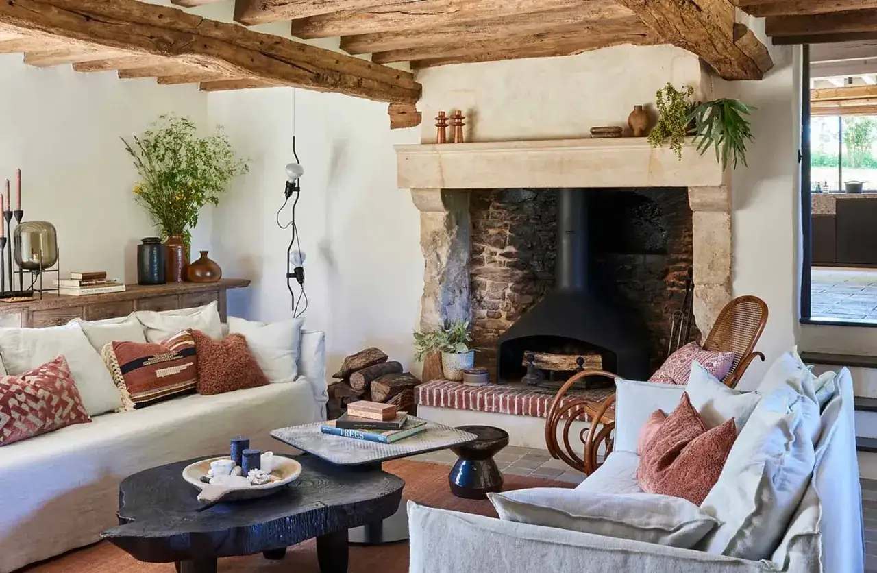 Accogliente soggiorno con camino in pietra, travi a vista e divani bianchi. Perfetto arredamento casa campagna per un rifugio rilassante.