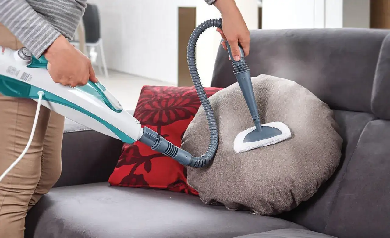 Come pulire divano in microfibra con un pulitore a vapore. La persona pulisce un cuscino rotondo sul divano.