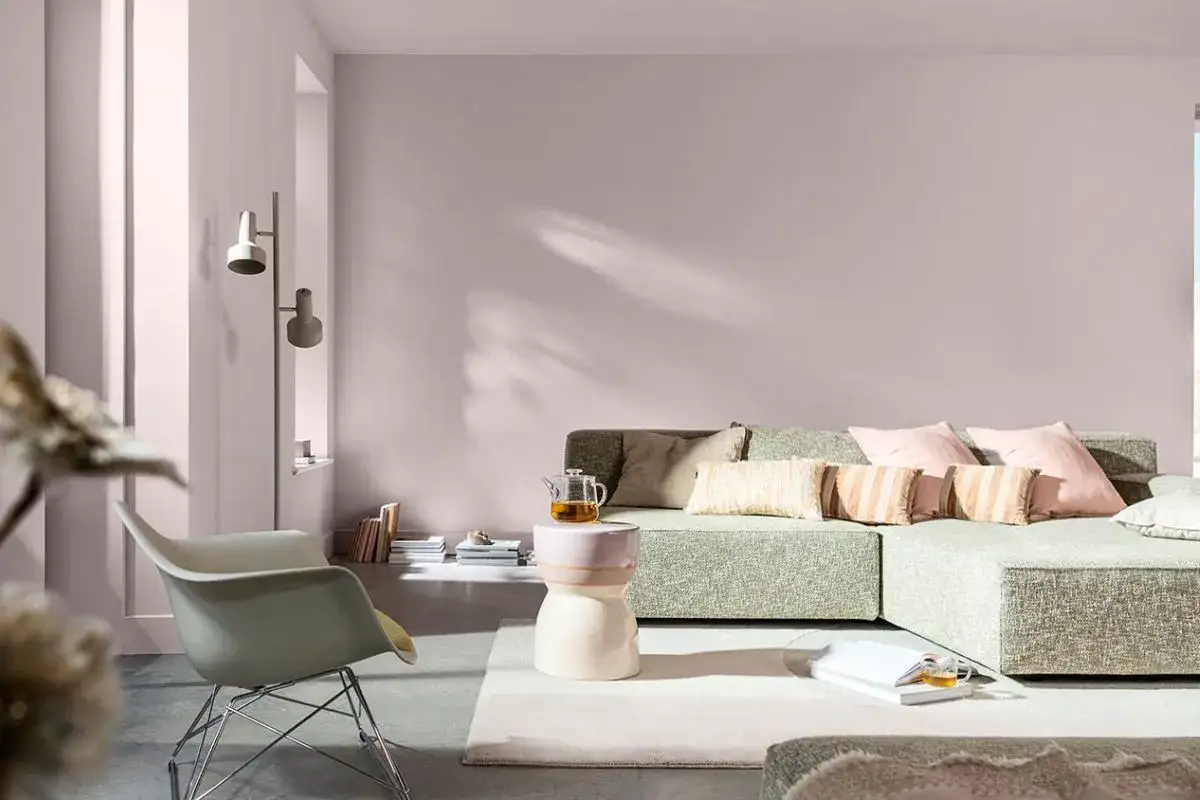 Salotto con divano modulare verde, poltrona chiara e tavolino. Le pareti rosa cipria e i cuscini rosa e beige evocano colori primaverili.