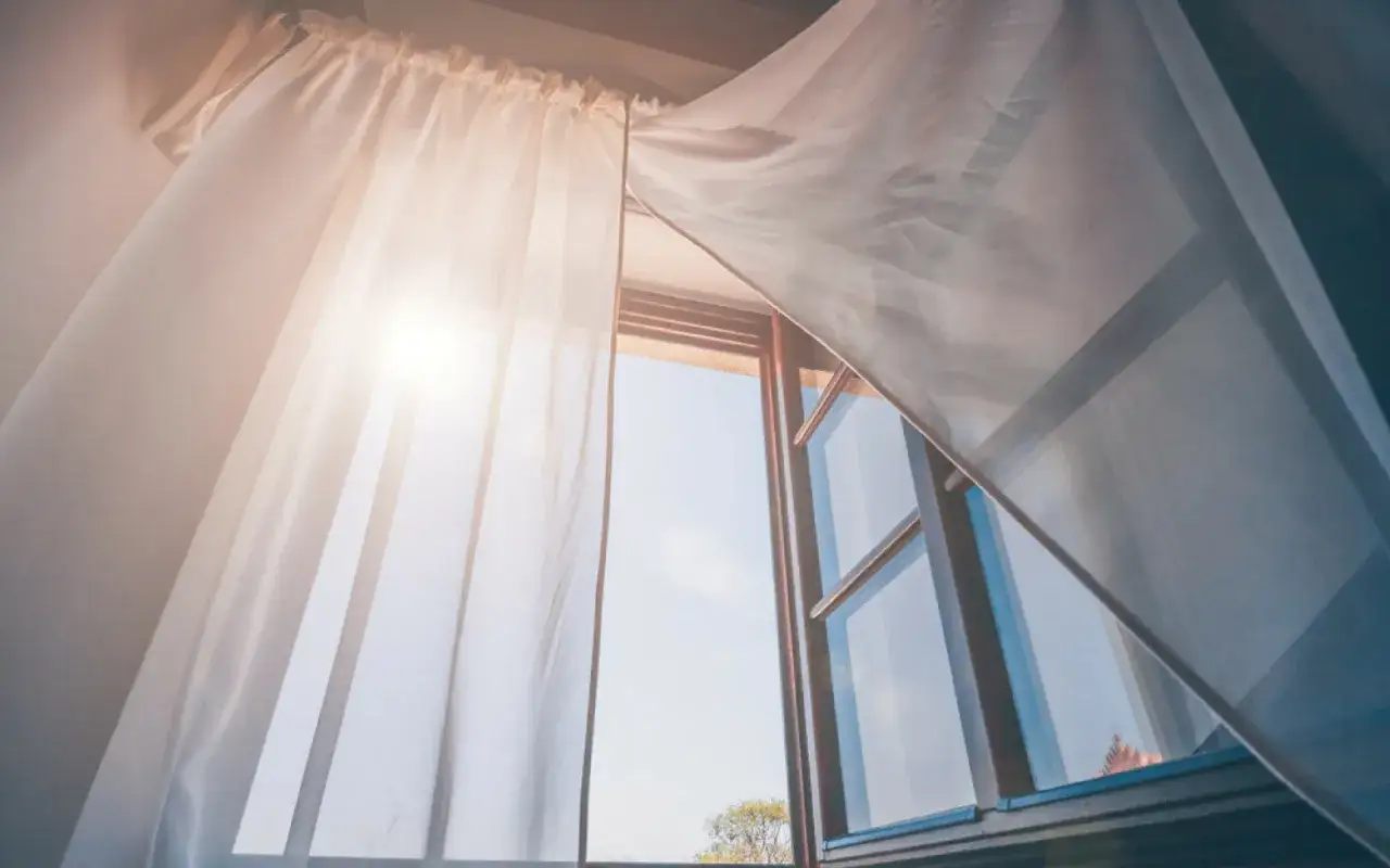 Tende bianche svolazzano con la brezza che entra da una finestra aperta, un modo naturale per eliminare gli odori in casa.
