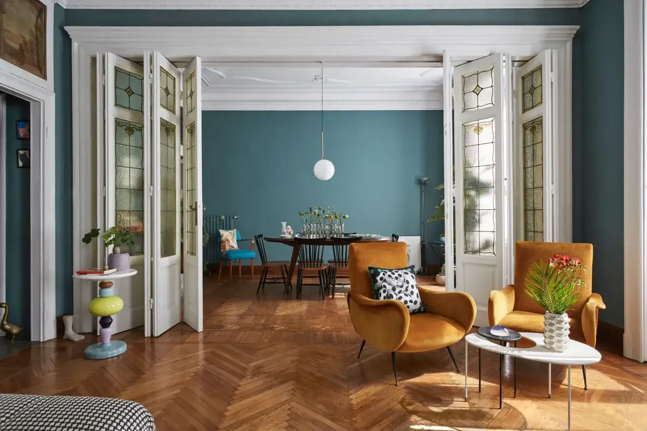 Soggiorno con poltrone ocra, tavolino colorato e sala da pranzo sullo sfondo. Ottime idee arredo per un ambiente accogliente.