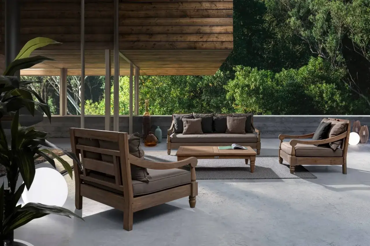 Un set da esterno in legno con divano e poltrone, stile divano bali, su una terrazza con vista su un giardino lussureggiante.