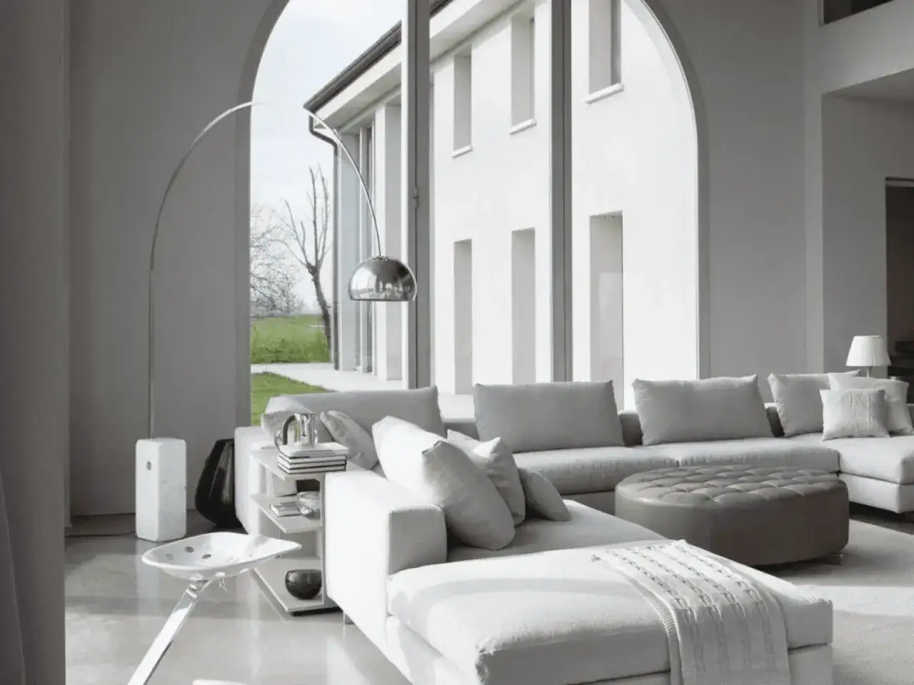 Soggiorno minimalista con divano modulare bianco, pouf in pelle e lampada ad arco. Perfetto per arredare casa moderna con stile.