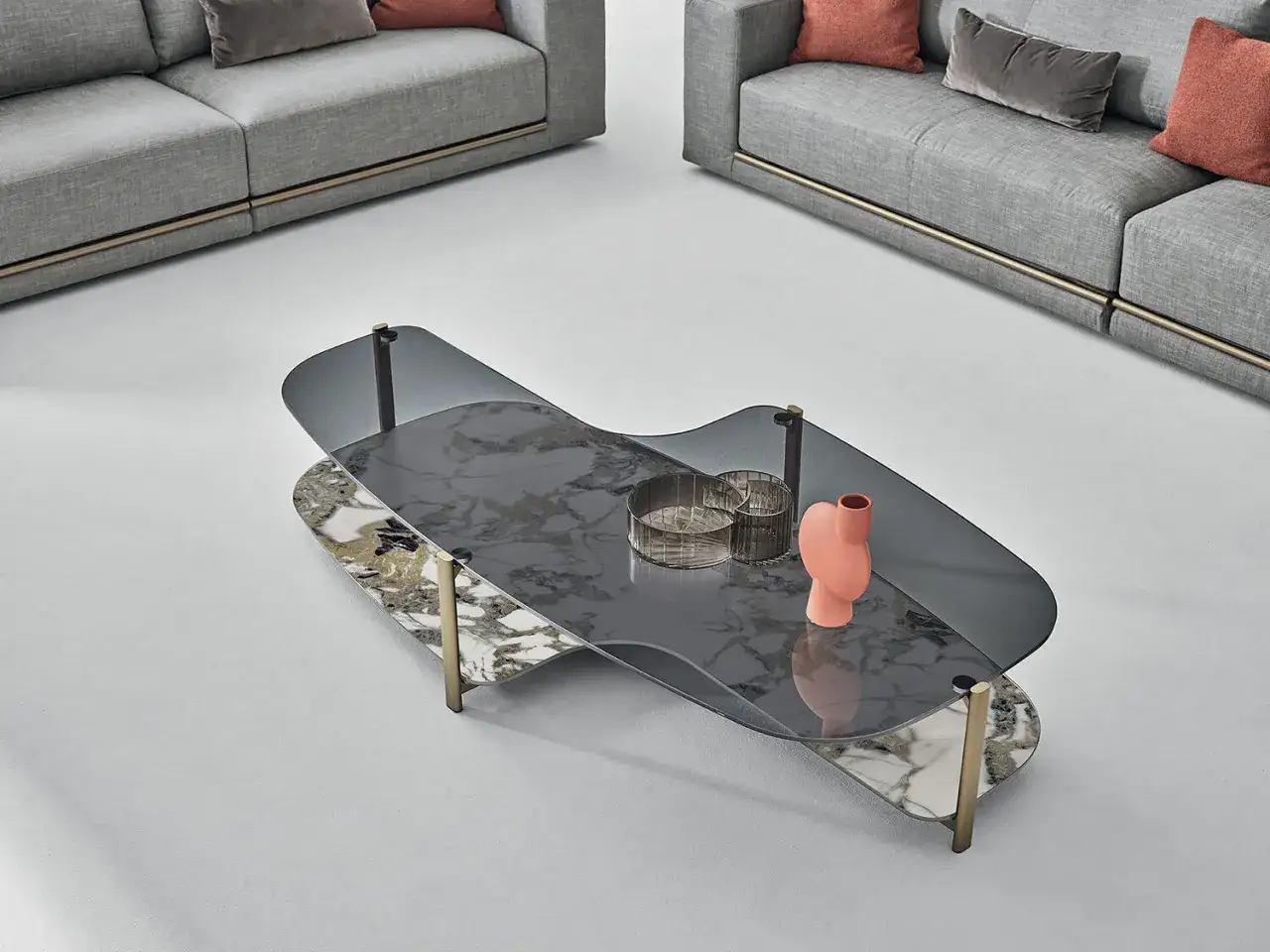 Un tavolino moderno con piano in vetro fumé e marmo, decorato con un vaso corallo e due portacandele. Perfetto per arredare il salotto, offre idee su cosa mettere sul tavolino del salotto.