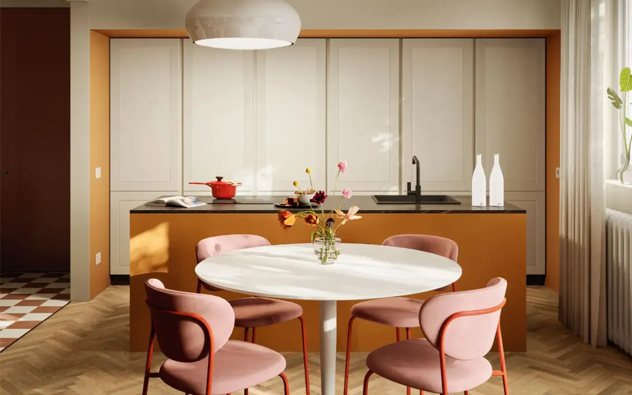Un tavolo rotondo con sedie rosa accoglienti, un'isola cucina color ocra e un vaso di fiori creano un'atmosfera clara bona e invitante.