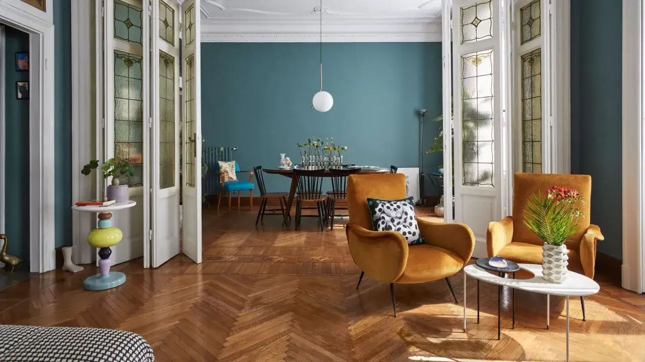 Soggiorno con arredamento misto moderno e antico: poltrone ocra, tavolino colorato, porte a vetri e parquet.