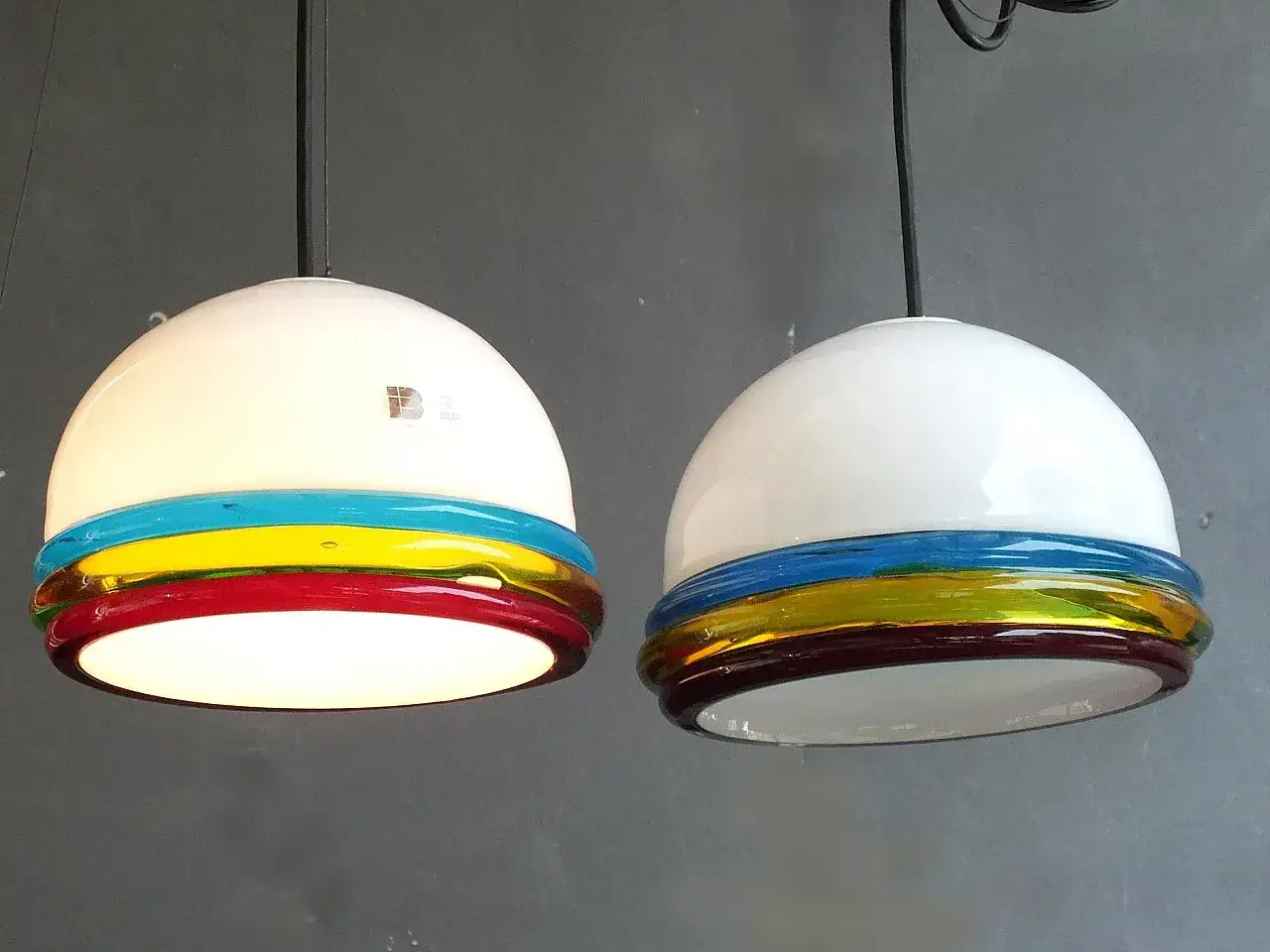 Due lampade a sospensione in vetro bianco con fasce colorate (blu, giallo, rosso) che creano un effetto arcobaleno. Itre illuminazione di design.