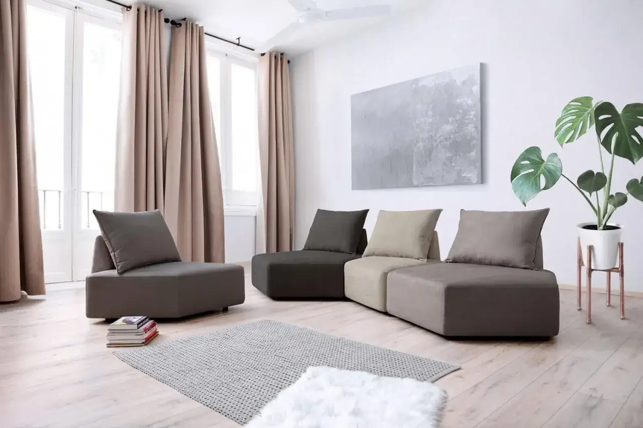 Un soggiorno moderno con un divano modulare grigio e beige, un tappeto chiaro e un pavimento in legno chiaro.