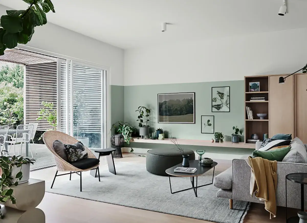 Soggiorno moderno con pareti verdi e bianche, mobili in legno chiaro, divano grigio e poltrona in rattan. Un esempio di come abbinare il verde con stile.