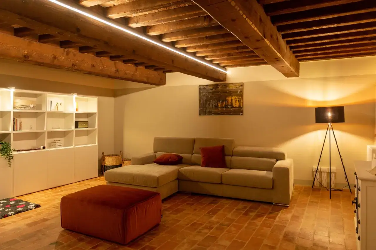 Illuminazione sopra divano crea un'atmosfera accogliente. Divano angolare beige, pouf rosso, libreria bianca e lampada da terra.