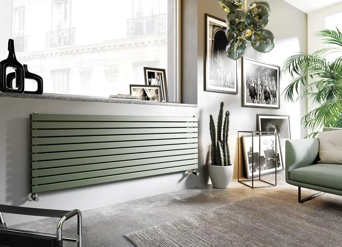 Un moderno termosifone orizzontale color salvia, perfetto per arredare parete con stile. Accanto, cactus e foto d'epoca creano un angolo accogliente.