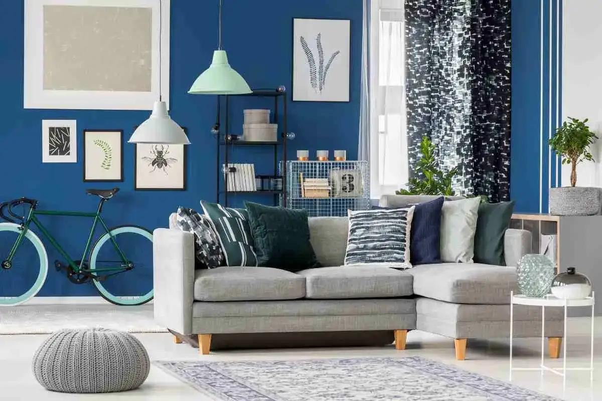 Un soggiorno moderno con divano grigio, cuscini a fantasia e una bicicletta verde. La parete blu intenso crea un'atmosfera con colori freddi.