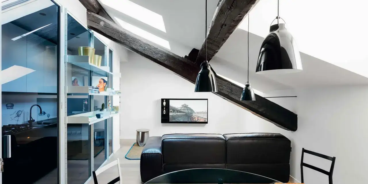 Luminoso appartamento mansardato con travi a vista, cucina moderna a vista e un accogliente soggiorno con divano in pelle.
