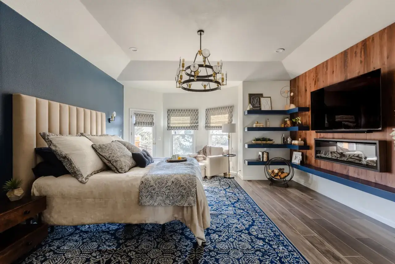 Elegante camera da letto blu e beige con letto king-size, camino moderno e TV a parete.