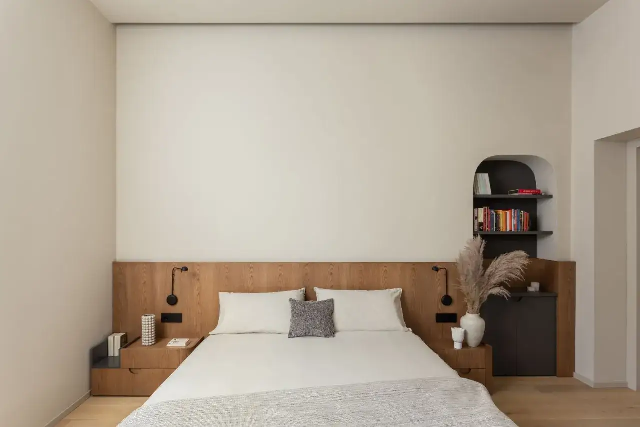 Camera da letto bianca con testiera in legno, comodini, libreria ad arco e decorazioni naturali. Ottime idee per una camera da letto bianca.