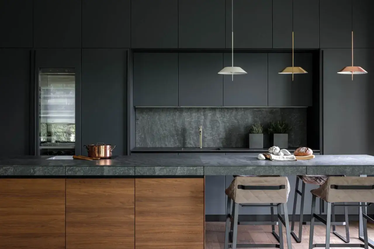 Cucina moderna Valcucine Spa con isola in legno e pietra, bancone con sgabelli e illuminazione di design.