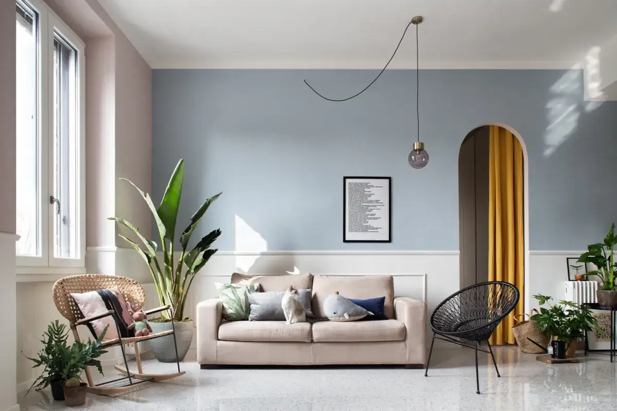 Soggiorno con pareti color pastello e azzurro polvere, divano beige, poltrona in rattan e dettagli che ispirano idee pareti colorate particolari.