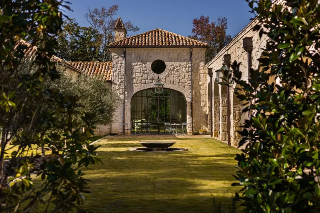 Giardino con fontana e casa di campagna in pietra, con tetto in tegole rosse. Idee case di campagna esterni con un grande arco vetrato.