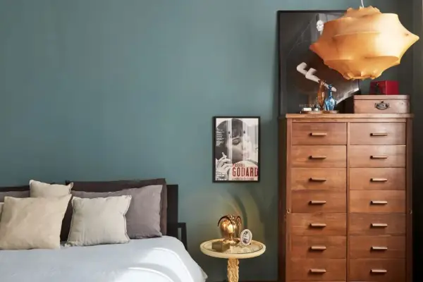 Un'elegante camera da letto con pareti color ottanio, un letto con cuscini in lino e un comò in legno. L'abbinamento colori camera da letto è sofisticato e rilassante.