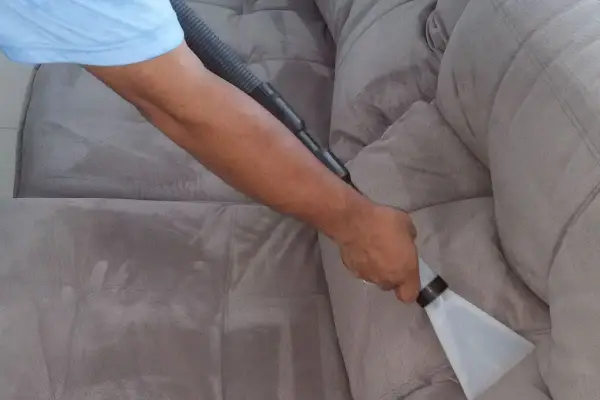 Un braccio usa un aspiratore per pulire un divano in tessuto grigio. Il processo di come pulire divano in tessuto è mostrato in dettaglio.