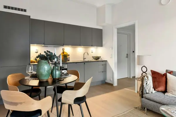 Arredare una sala moderna con cucina a vista: tavolo rotondo con sedie in legno, vasi verdi e candele.