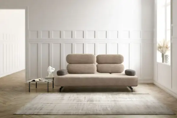 Un elegante divano beige, un'opera d'arte di design, domina la scena. Accanto, un tavolino con libri e una scultura moderna.