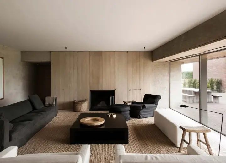 Elegante salone moderno con divani scuri, camino a parete in legno, tavolino nero e poltrona. Un esempio di come arredare un salone con stile minimalista.